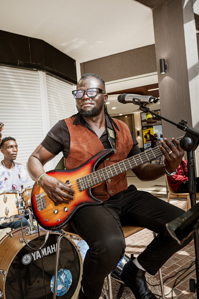 Bassist playing an electric bass with other musicians visible behind him