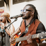 Bassist singing into a microphone while another vocalist performs behind him