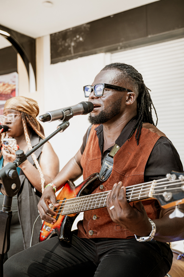 Bassist singing into a microphone while another vocalist performs behind him