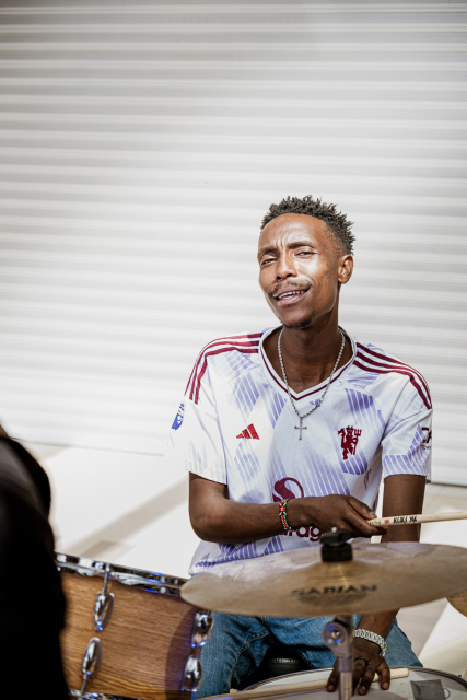 Drummer seated behind a drum kit and looking toward the camera.