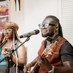 A bassist plays beside a singer during a live mall performance.