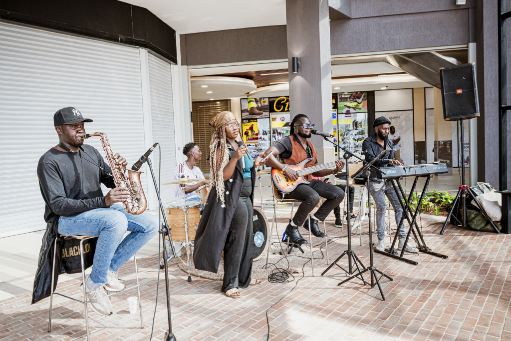 A five-member band performs together in an open mall area.