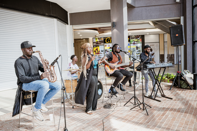 A five-member band performs together in an open mall area.