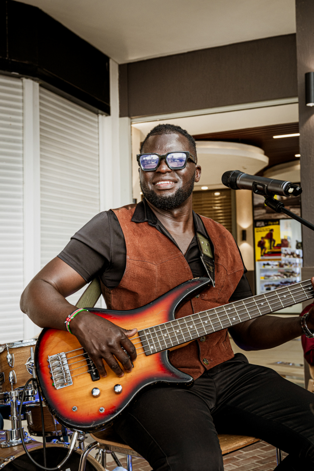Smiling bassist holding a sunburst electric bass beside a microphone.