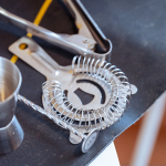 Cocktail strainers, tongs, and other metal bar tools arranged on a work surface.