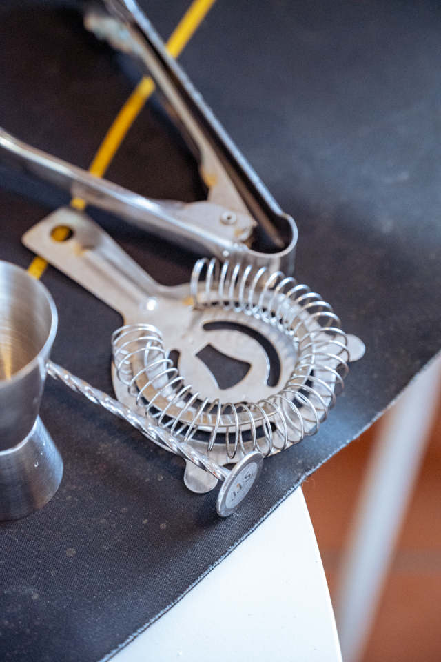 Cocktail strainers, tongs, and other metal bar tools arranged on a work surface.