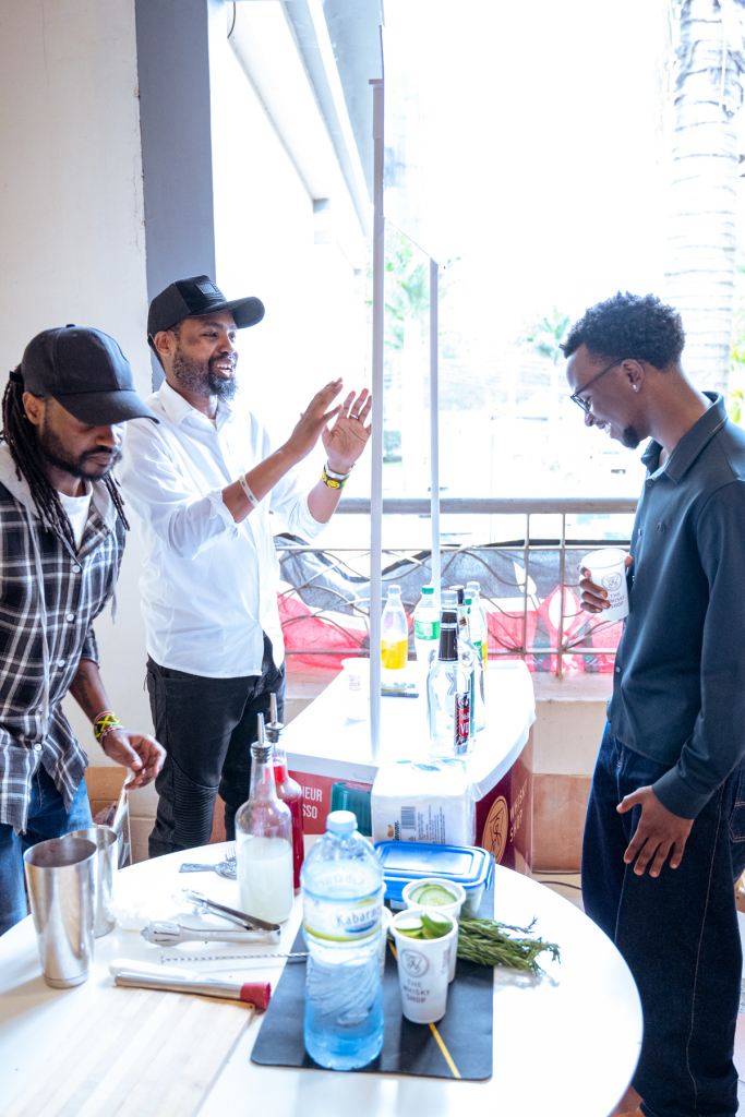 Three people interact beside a tasting counter as one man gestures and another holds a cup.