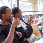 Two guests sit together holding tasting cups near the mall windows