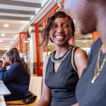 Smiling woman seated at a table inside the shopping mall while another attendee is visible in the foreground
