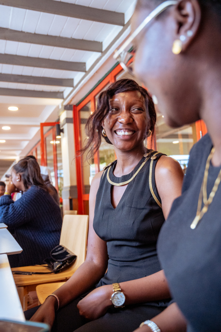 Smiling woman seated at a table inside the shopping mall while another attendee is visible in the foreground