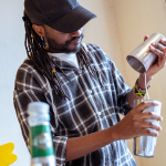 Bartender pouring a drink into a tall glass while bottles sit in the foreground