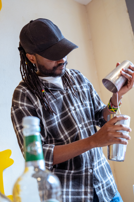Bartender pouring a drink into a tall glass while bottles sit in the foreground