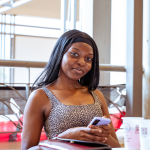 Woman smiling while holding a smartphone at a table in a bright indoor atrium