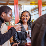 Smiling woman in a black leather jacket speaks with another guest at the table.