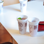 Branded takeaway cups arranged on a white table, including a cup with a green garnish.