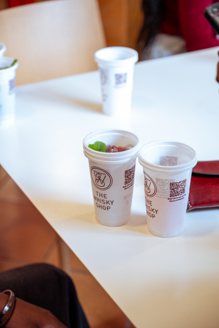 Branded takeaway cups arranged on a white table, including a cup with a green garnish.