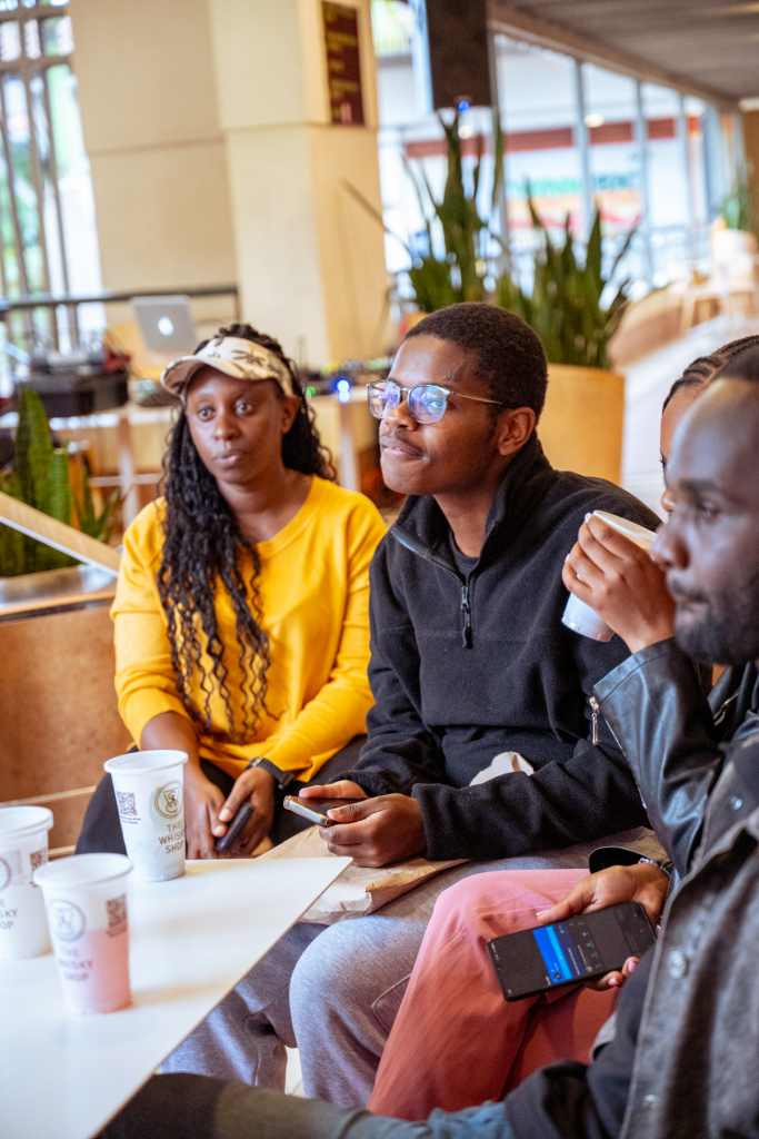 Three attendees sit together at a table with tasting cups in a shopping mall setting