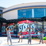 DZ6 1226 Performers raise their arms in formation outside a shopping mall entrance.