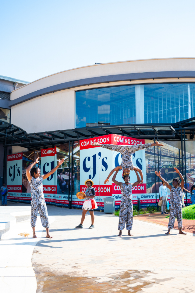 DZ6 1226 Performers raise their arms in formation outside a shopping mall entrance.