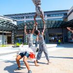 DZ6 1241 Performers create an acrobatic formation in the mall plaza, with one performer lifted above the others.