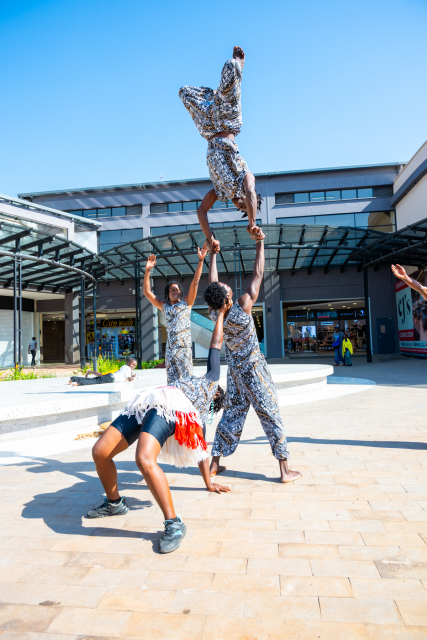 Performers create an acrobatic formation in the mall plaza, with one performer lifted above the others.