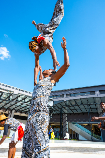 A performer is lifted overhead by another performer in the mall plaza.