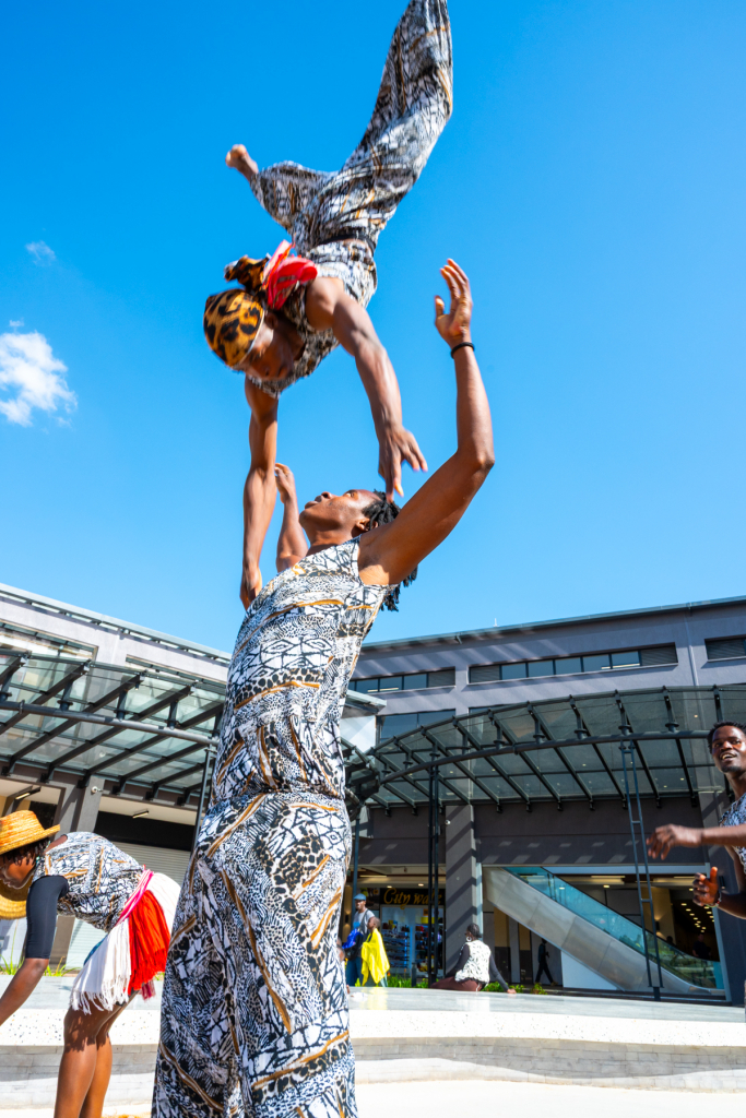 A performer is lifted overhead by another performer in the mall plaza.