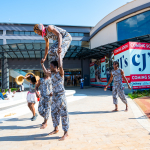 DZ6 1258 A group of performers presents an acrobatic routine in the mall courtyard with storefronts behind them.