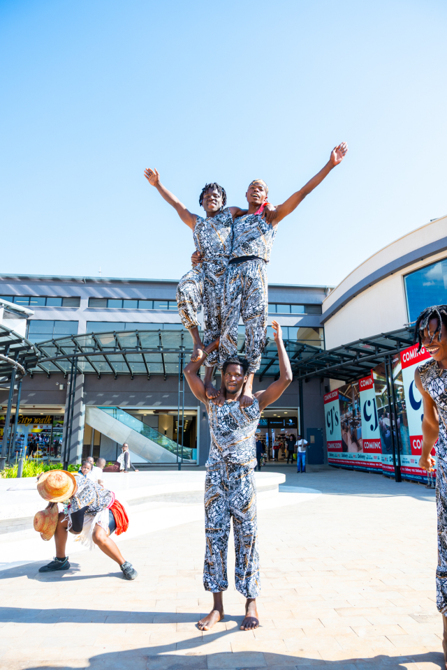 DZ6 1263 Performers in matching patterned outfits form a human acrobatic pose outside the shopping mall.