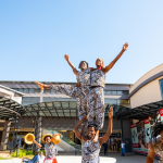 DZ6 1265 Performers create a tall human pyramid outside the shopping mall while other performers stand nearby.