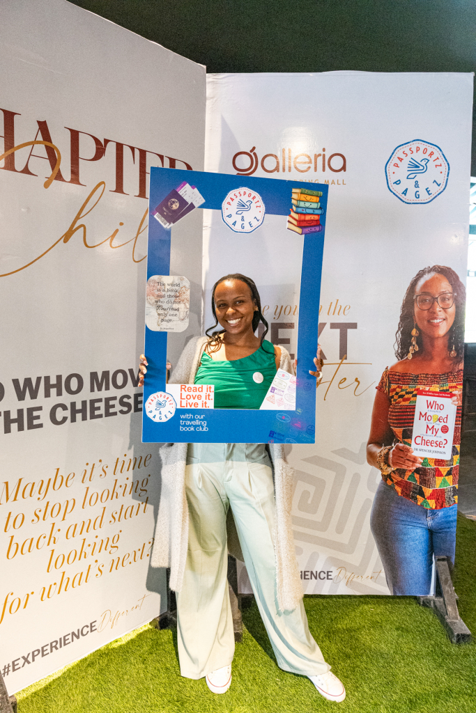 Smiling woman poses inside a blue book-themed photo frame while another woman holds a matching sign.