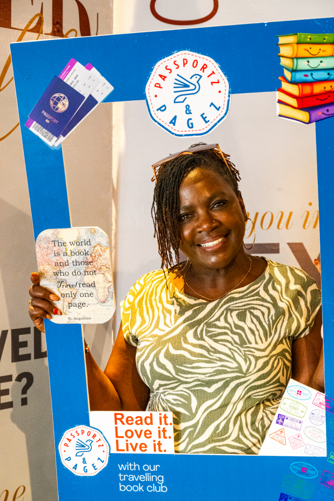 Smiling woman holds a blue reading-themed photo frame decorated with books, passports, and event graphics.