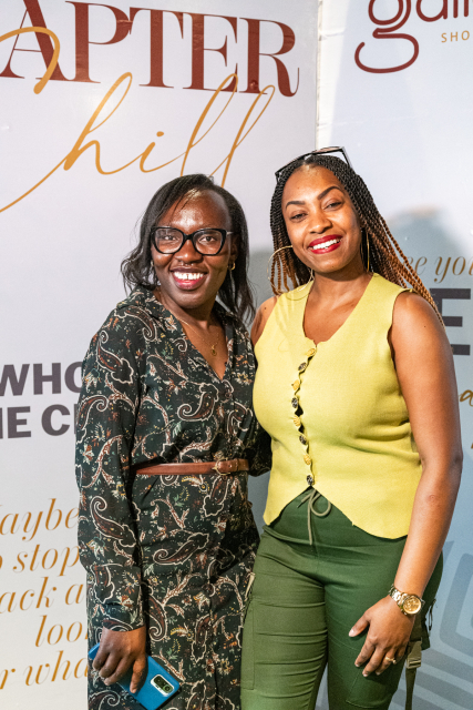 Two smiling women pose together in front of a white backdrop with literary-themed text and mall branding.