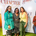 DZ6 1775 Three women smile together between branded backdrop panels at a mall event.
