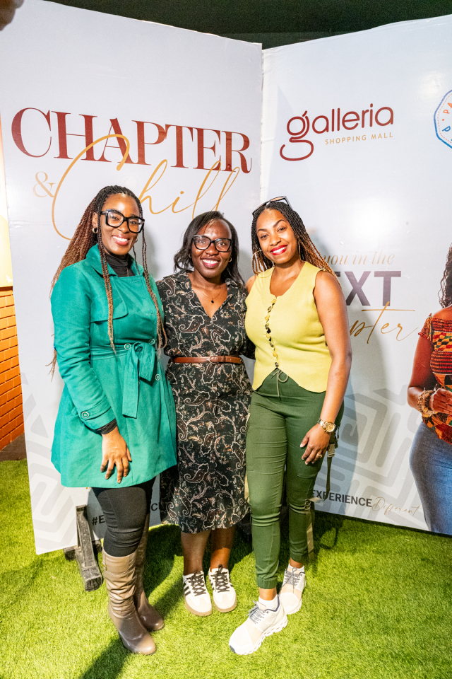 DZ6 1775 Three women smile together between branded backdrop panels at a mall event.