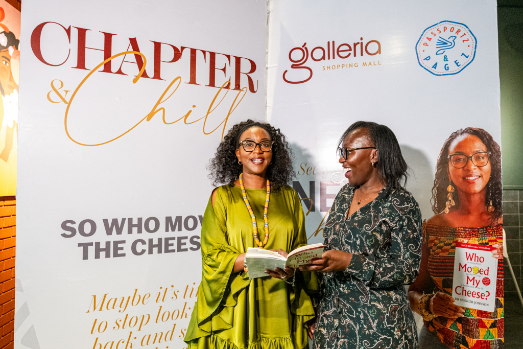 Two women exchange an open book in front of a Chapter & Chill and Galleria backdrop.
