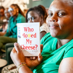 DZ6 2035 A woman in green holds up the book Who Moved My Cheese? while other guests sit behind her