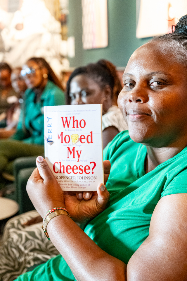 DZ6 2035 A woman in green holds up the book Who Moved My Cheese? while other guests sit behind her