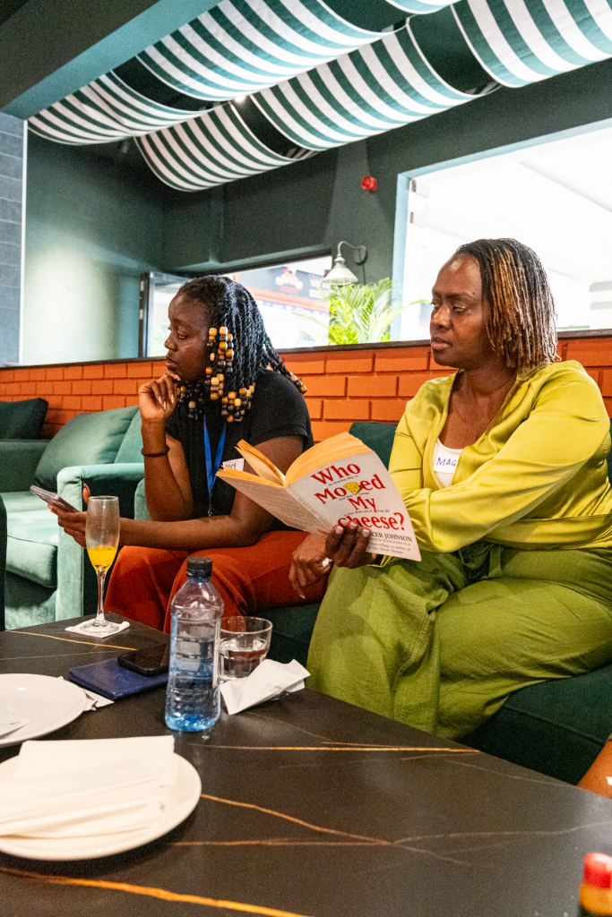 Two women sit together on a sofa while one holds an open book.