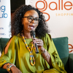DZ6 2137 Woman in green speaks into a microphone while seated at a Galleria Shopping Mall event.