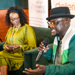DZ6 2193 Smiling man in a hat speaks into a microphone and gestures during a panel discussion.