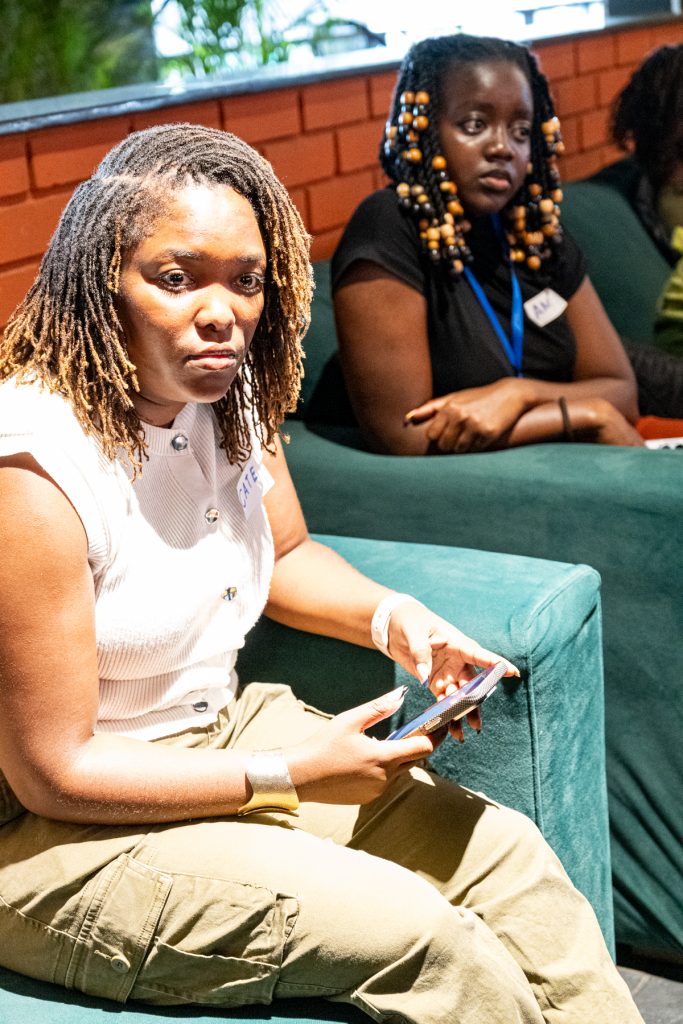 A seated woman looks at a phone while another attendee sits behind her on a sofa.