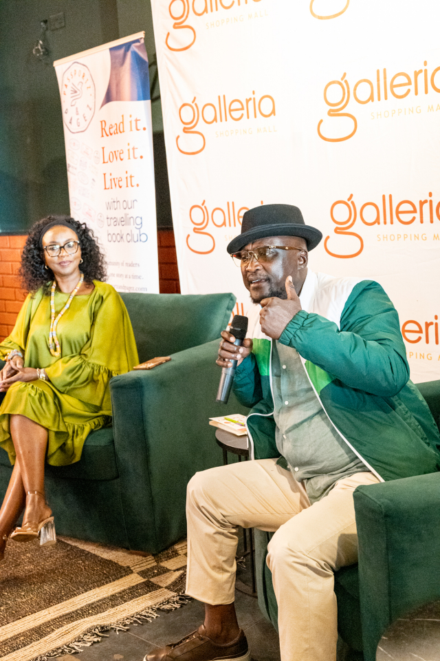 DZ6 2254 A man wearing a hat speaks into a microphone while seated beside a listening woman at a mall event.