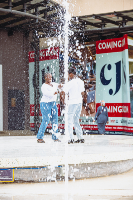 Two dancers perform on an outdoor stage as a fountain sprays in front of them.
