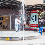 Fountain and Mall Courtyard A fountain sprays in front of mall storefronts and people gathered in the courtyard