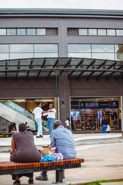 Two spectators watch dancers performing on a stage outside the shopping mall.