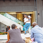 Spectators Watching a Dancer on Stage Spectators watch a dancer performing on an outdoor stage near an escalator.