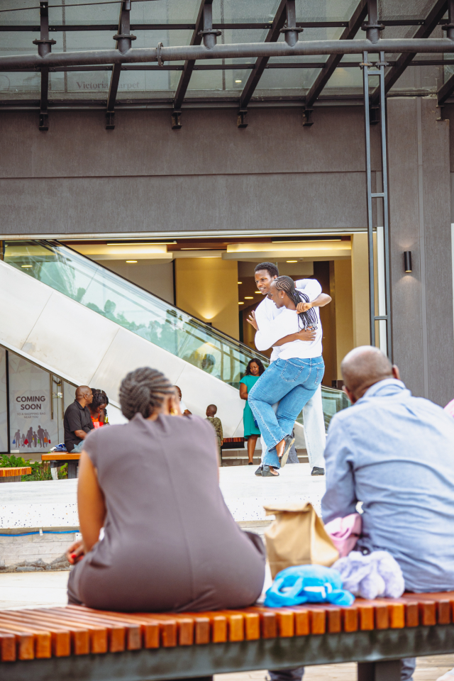 Spectators Watching a Dancer on Stage Spectators watch a dancer performing on an outdoor stage near an escalator.